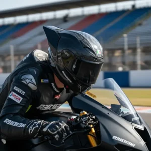 A motorcycle racer tucked behind a windscreen, highlighting the aerodynamic spoiler and intake vents of a racing helmet.