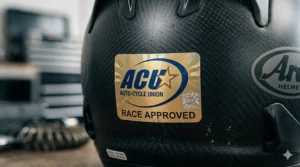 Detailed view of a gold ACU sticker on a full-face helmet, indicating it is approved for racing on British circuits.
