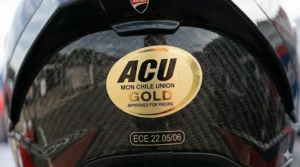 Detailed macro shot of the metallic gold ACU sticker found on motorcycle helmets approved for UK racing.