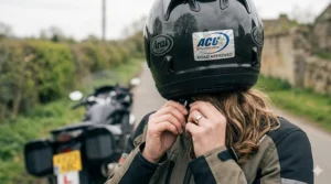 A pillion rider putting on a road-legal helmet with a clear ACU Silver rating for UK motorway travel.