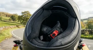 Underneath view of a motorcycle helmet showing the plush comfort liner and the red micrometric buckle chin strap fastening common in the UK market.