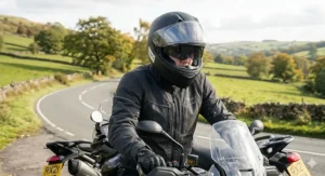 A motorcyclist riding a touring bike on a winding UK country road, wearing a SHARP 5 star rated helmet with the sun visor deployed to manage glare.