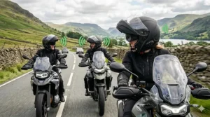 Three motorcyclists riding Triumph motorbikes in formation along a lakeside road in the UK, with green graphic overlays illustrating the rider-to-rider Bluetooth intercom connection.