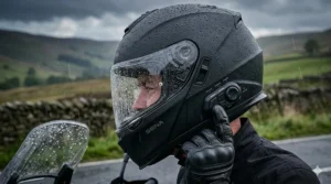 Close-up of a waterproof Bluetooth helmet covered in raindrops during a downpour on a British country road, proving its weatherproofing capabilities.