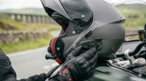 A rider wearing a black leather glove uses the large buttons on a motorbike intercom helmet.