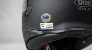 Product shot of the black full-face Shoei helmet with vlogging integration diagrams for camera and audio.