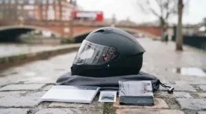 The matte black polycarbonate helmet resting on its grey microfibre drawstring storage bag, accompanied by the user manual, anti-fog cloth, and spare Pinlock lens.