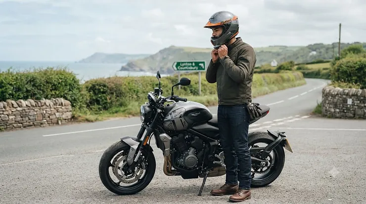 A rider adjusting a certified Kevlar motorcycle helmet on a British road, showcasing premium safety gear for UK riders. Kevlar motorcycle helmet