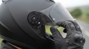 Hands demonstrating the quick-release pin mechanism for swapping a motorcycle helmet visor.