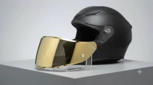 A detailed close-up studio photograph of the matte black AGV motorcycle helmet. The silver mirror visor is replaced by a highly reflective, gold iridium mirror visor, which is presented on a clear acrylic stand in the foreground. The gold coating shows a warm, distinct sheen, contrasting with the cool tones of the helmet shell.