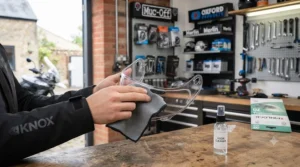 A rider gently cleaning a removed universal Pinlock insert with a microfibre cloth and lukewarm water to maintain optical clarity.