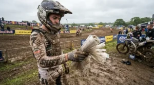 A rider holding a tear-off visor pack trackside at a muddy British motocross race day